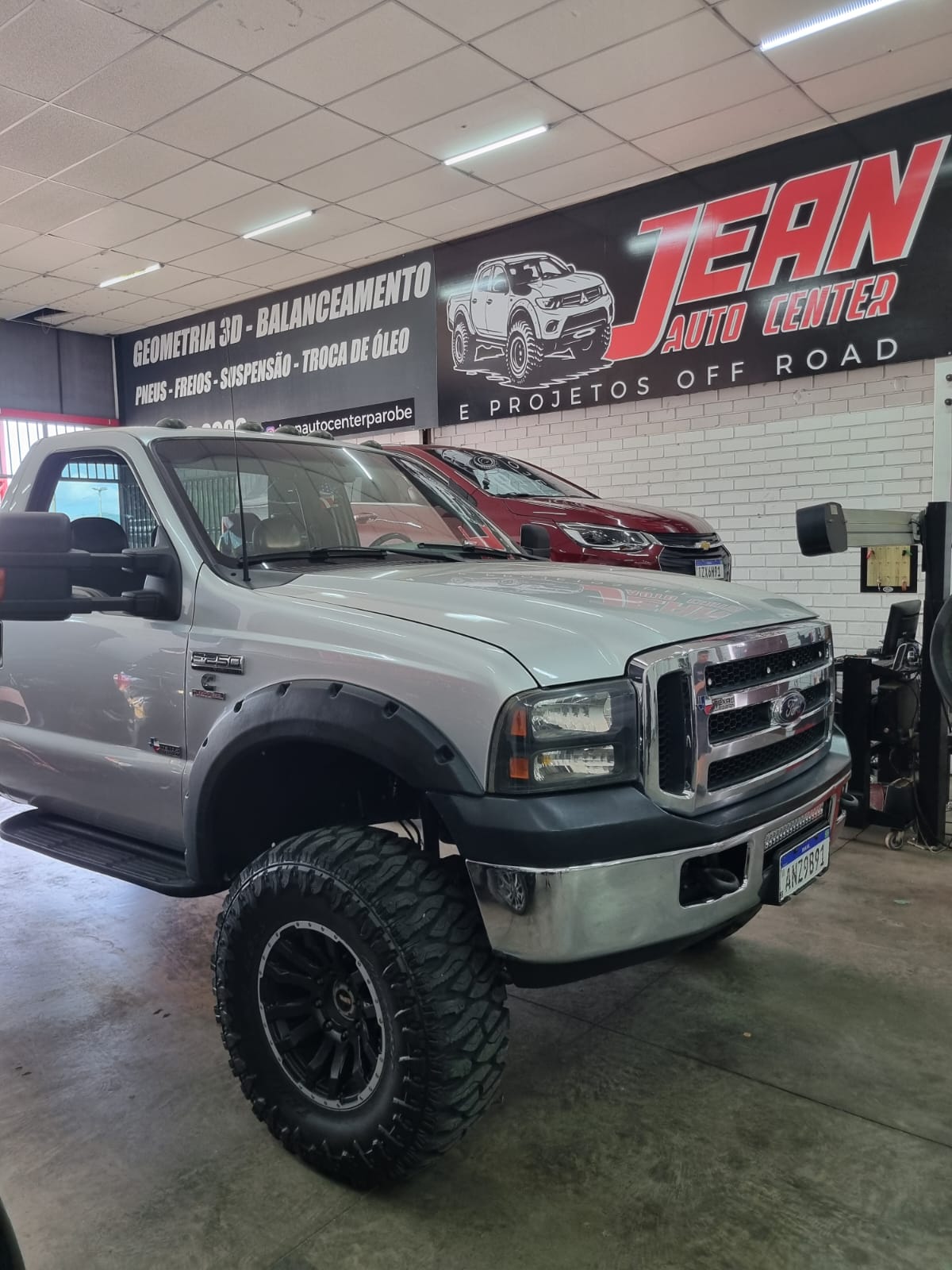 Ford F-250 branca, vista frontal, suspensão elevada e pneus off-road na oficina