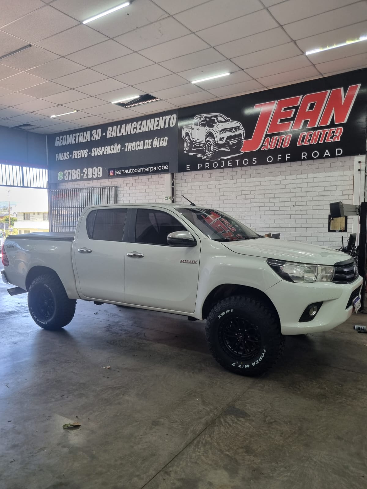 Toyota Hilux branca com suspensão elevada e rodas pretas, vista frontal