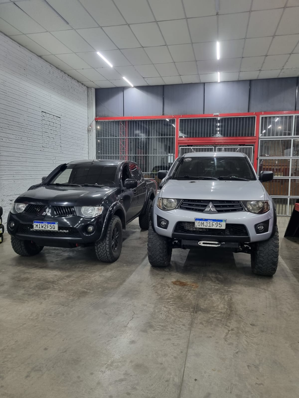 Duas caminhonetes Mitsubishi L200 Triton, preta e branca, com suspensão elevada lado a lado