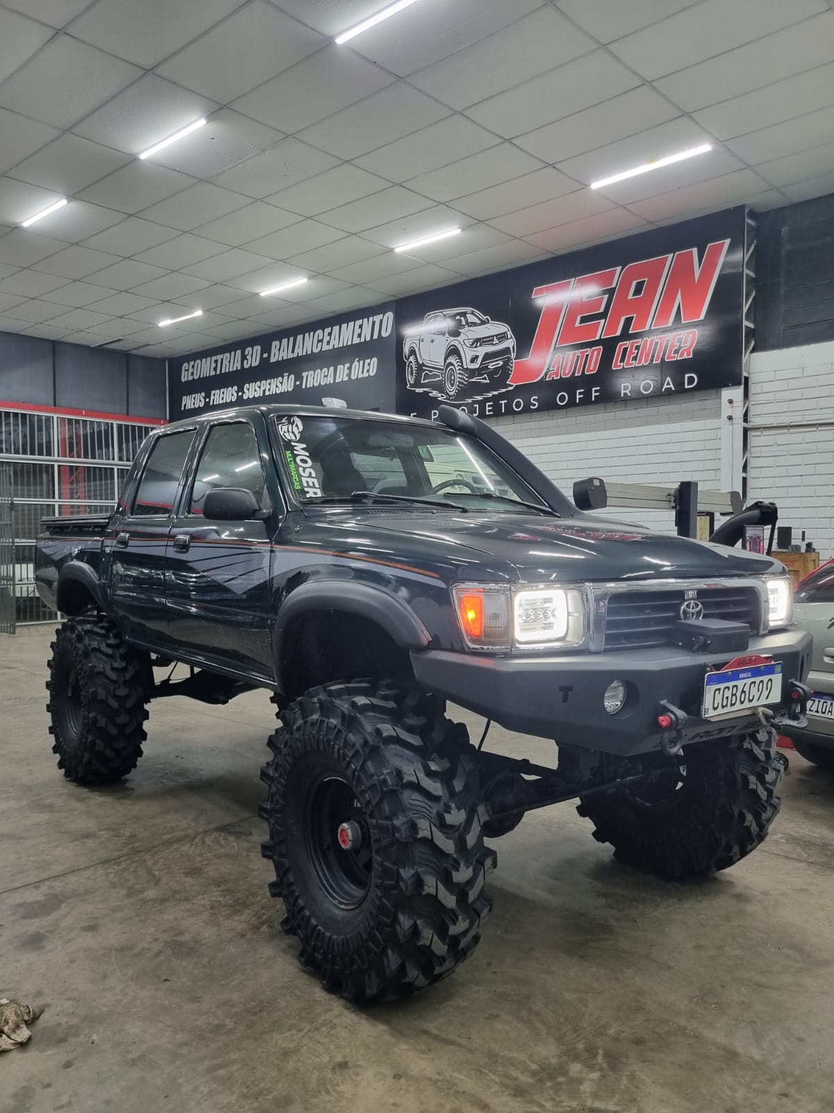 Picape 4x4 extrema preta com pneus enormes tipo rock crawler e para-choque reforçado