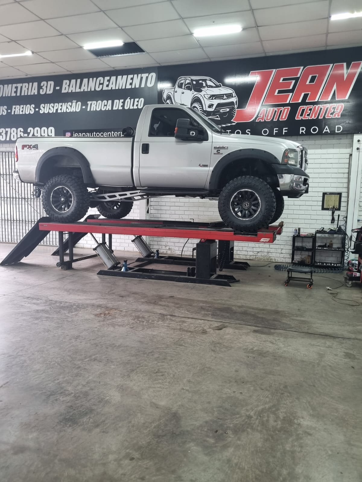 Ford F-250 branca no elevador durante geometria e alinhamento 3D após lift de suspensão